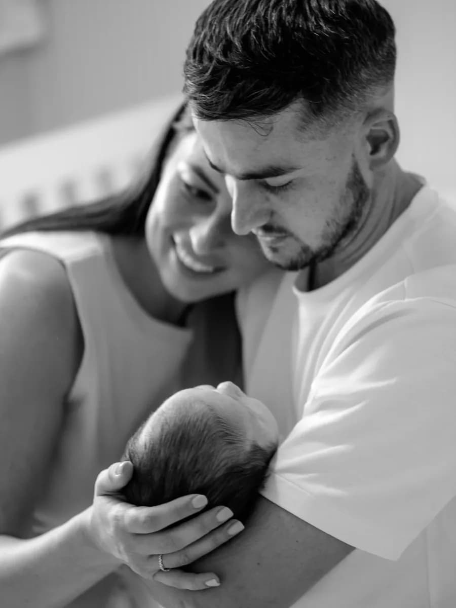 A man and woman cradling a newborn baby together, faces close as they look down at the infant