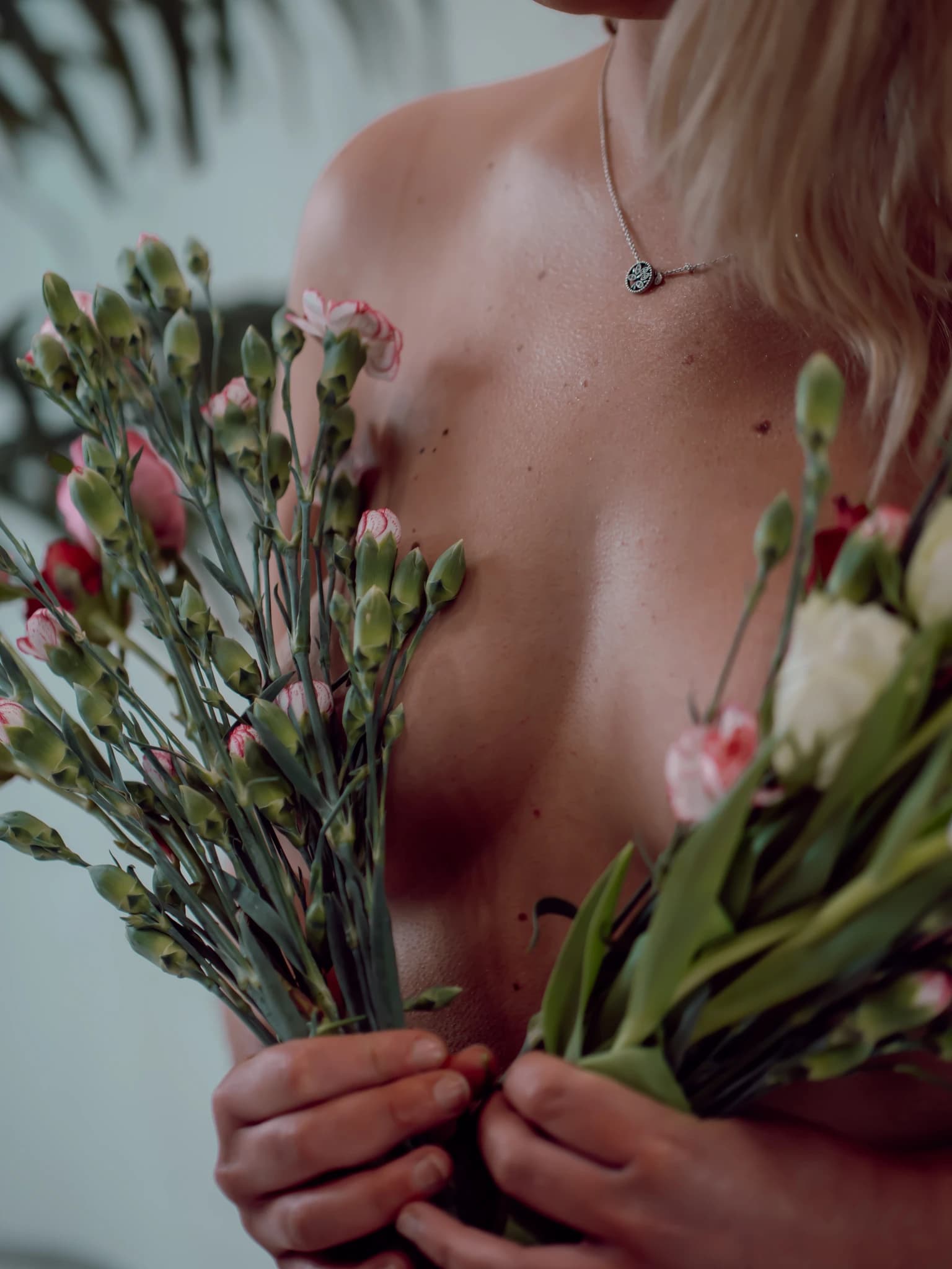 Woman holding bunches of pink and green carnation buds in front of her face, wearing a pendant necklace