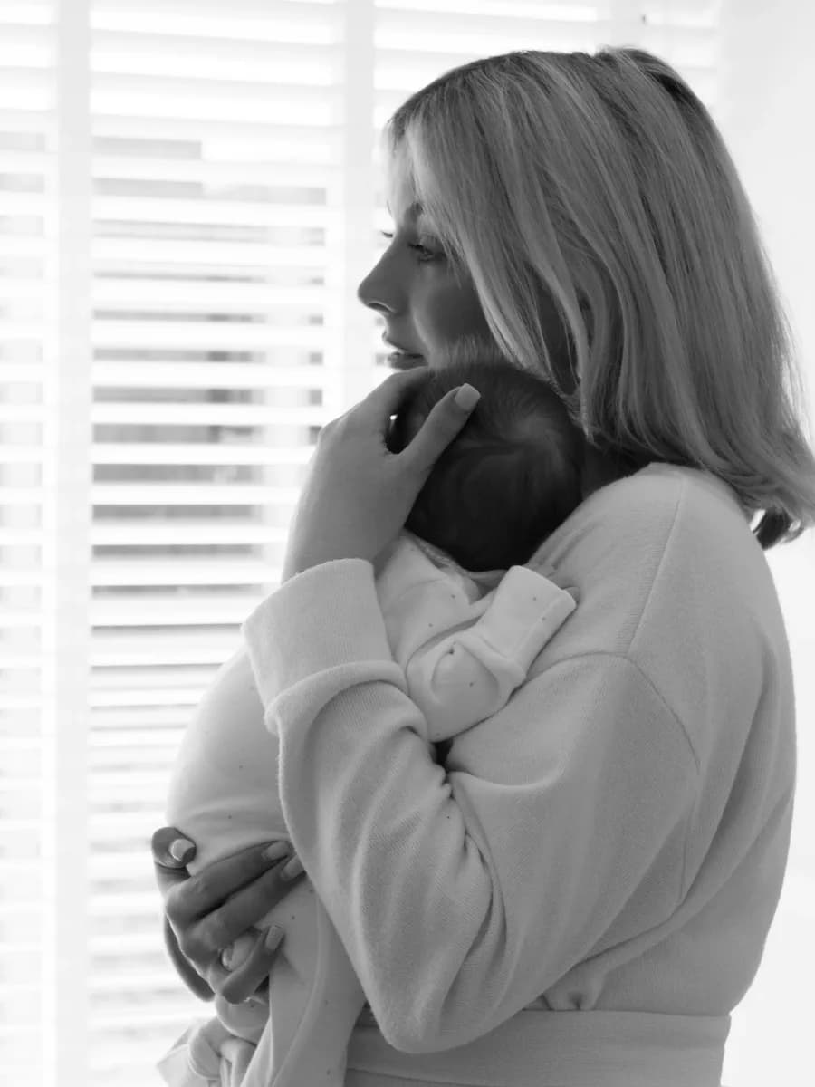 Woman in profile holding a baby against her shoulder, both facing away from the camera
