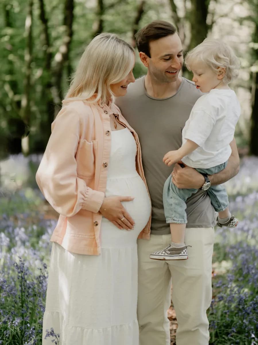 A man holding a small child stands next to a pregnant woman among purple flowering plants