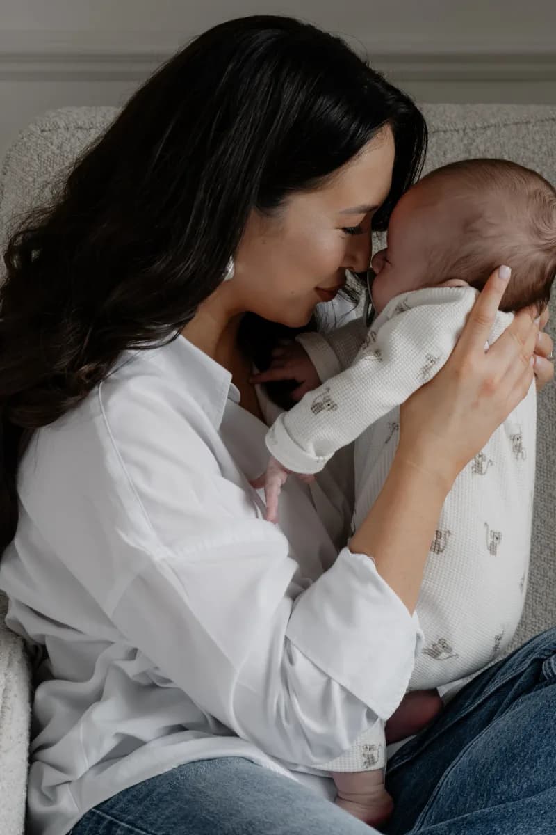 Woman in white shirt holding a newborn baby wrapped in white cloth against her shoulder