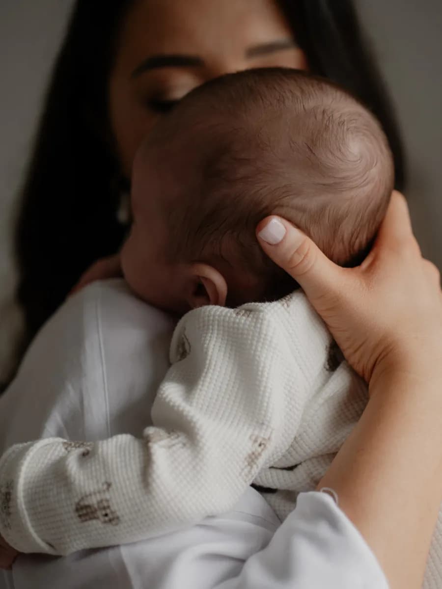 A woman holding a baby against her shoulder, the baby's face not visible as it rests against her neck